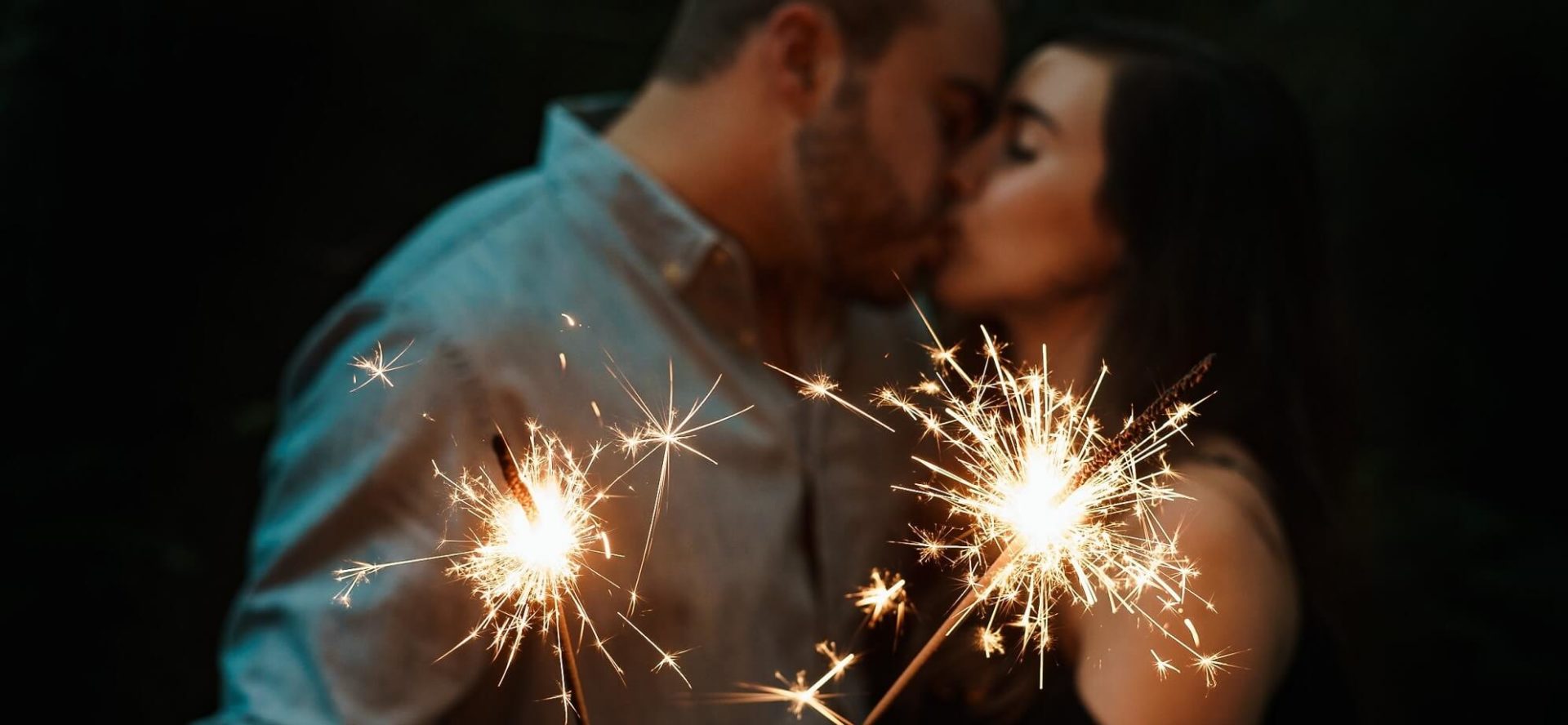 man and woman kiss at night with sparklers