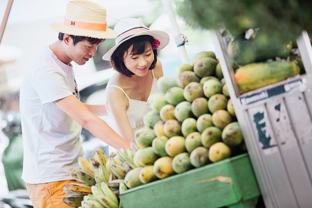 asian man and woman bend down to look at fruit on a fruit cart